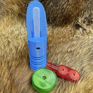 May include: A blue plastic tool with a white insert, a green disc with text, and a red plastic clip. The objects are arranged on a brown, furry surface. The blue tool has a cylindrical base.