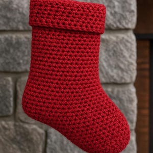 May include: A bright red crochet Christmas stocking featuring a thick, folded cuff at the top. The stocking is constructed with a dense, uniform stitch pattern throughout the entire body, creating a textured appearance in a vibrant, solid red yarn.