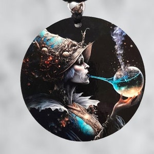 May include: A round pendant necklace with a black cord and a black tassel. The pendant features a colorful illustration of a woman with a large hat blowing a bubble from a glass orb.