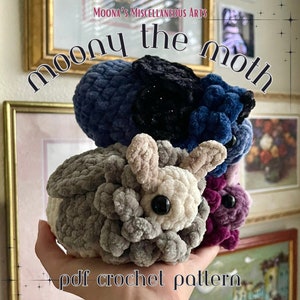 Könnte beinhalten: Ein Häkelmuster für ein Plüsch-Mottenspielzeug. Das Muster heißt "Moony the Moth" und ist als PDF-Download erhältlich. Das Bild zeigt eine Hand, die einen Stapel von vier gehäkelten Motten in verschiedenen Farben hält: grau, weiß, blau und lila.