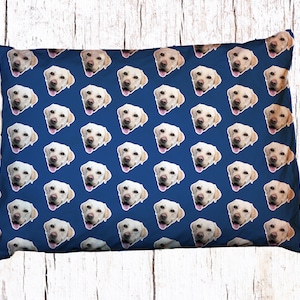 May include: A blue pillow with a repeating pattern of a dog's face. The dog has white fur and is looking directly at the camera.