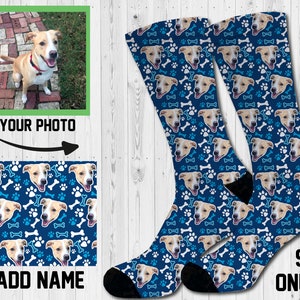 May include: A pair of blue socks with a white paw print and bone pattern. The socks feature a repeated image of a dog's face. The socks are available in one size, 9-11. "Add Name" and "Your Photo" are written on the image.