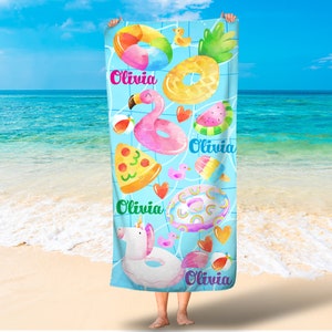 May include: A blue beach towel with a colorful design featuring various inflatable pool toys, including a pineapple, a flamingo, a pizza slice, a unicorn, and a watermelon. The towel has the name "Olivia" printed on it four times.
