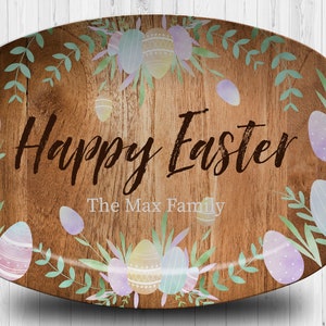 May include: A wooden oval serving platter with a rustic woodgrain design. The platter is decorated with a wreath of pastel Easter eggs and green leaves. The text "Happy Easter" and "The Max Family" is printed on the platter.