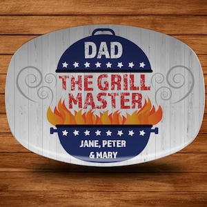 May include: White oval serving platter with a blue, red, and white design. The design features a grill with flames, the text "Dad The Grill Master", and the names "Jane, Peter & Mary".