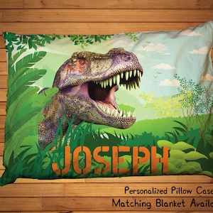 May include: A green and blue pillowcase with a dinosaur illustration and the name "JOSEPH" printed in orange.  Personalized Pillow Case Matching Blanket Available.