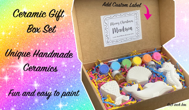 Pu&ograve; includere: Una scatola di cartone marrone con il coperchio aperto, che rivela un kit di pittura in ceramica. Il kit include un pennello, sei piccoli flaconi di vernice, un flacone di glitter e quattro figurine in ceramica a forma di coda di sirena, una conchiglia, un delfino e un cavalluccio marino. La scatola &egrave; etichettata "Ceramic Gift Box Set" e "Unique Handmade Ceramics". Il coperchio della scatola ha un'etichetta personalizzata che dice "Merry Christmas Madison".