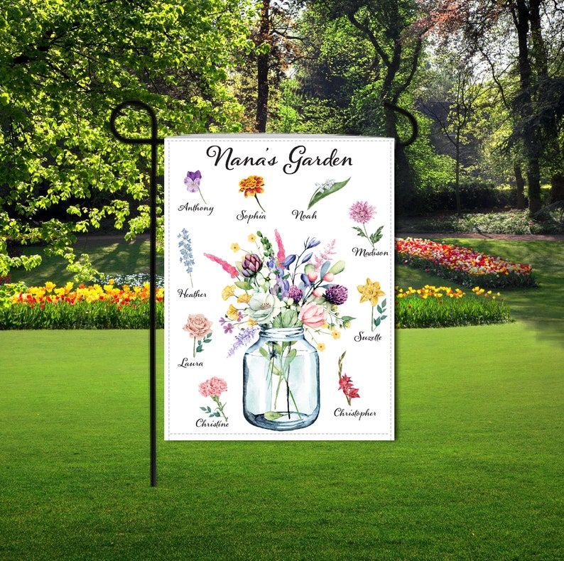 Op de afbeelding: Een witte tuin vlag met de tekst "Nana's Garden" bovenaan. Een aquarel illustratie van een glazen pot gevuld met verschillende bloemen. Elke bloem is gelabeld met een naam, zoals Anthony, Sophia, Noah, Madison, Heather, Laura, Christine en Christopher.