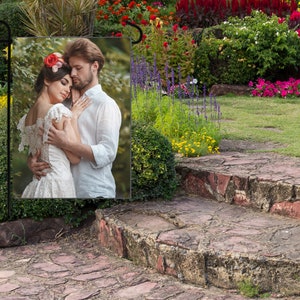 May include: A couple in love, the woman wearing a white lace dress and a flower crown, the man wearing a white shirt, standing in a garden setting.
