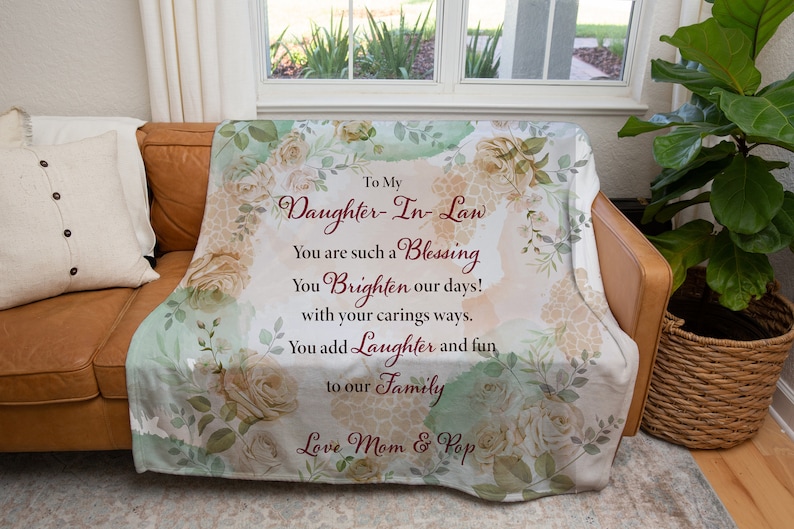 May include: A white throw blanket with a floral design and a message that reads "To My Daughter-In-Law You are such a Blessing You Brighten our days! with your carings ways. You add Laughter and fun to our Family Love Mom & Pop"