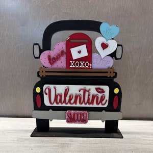 May include: A black wooden truck with a red mailbox and a white envelope with a red heart. The truck is carrying a variety of hearts with different messages, including "love", "be mine", "I love you", "cutie", and "XOXO". The truck has a red license plate that says "smooth".