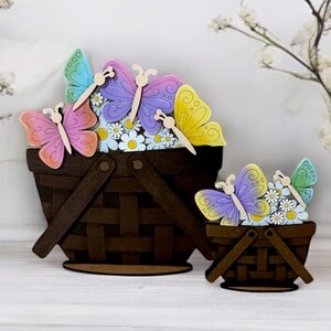 May include: Two wooden baskets filled with colorful butterflies and white flowers. The larger basket is brown with a woven pattern and the smaller basket is brown with a woven pattern. Both baskets have a wooden base.