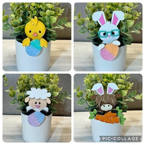 May include: Four white ceramic pots with green plants. Each pot has a different Easter-themed character holding an Easter egg. The characters are a yellow chick, a white bunny wearing glasses, a white lamb, and a brown horse with pink ears.