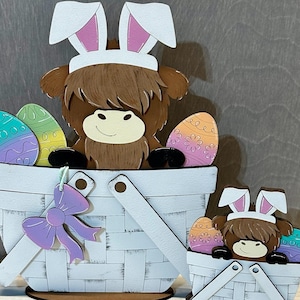 May include: Two wooden Easter bunny figurines with brown fur, white bunny ears, and pink accents. Each bunny is holding a basket filled with colorful Easter eggs. The larger bunny is holding a basket with a purple bow.