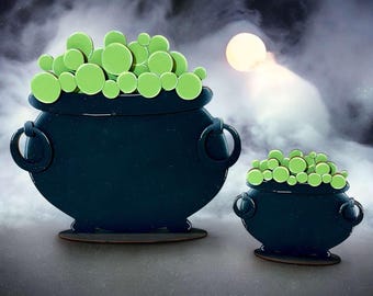 May include: Two black cauldron shaped Halloween decorations with green goo inside. The larger cauldron is in the foreground and the smaller cauldron is in the background.