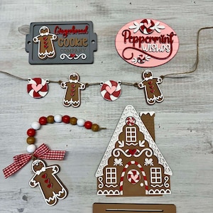 K&ouml;nnte beinhalten: Weihnachtsdekorationen zum Thema Lebkuchen, darunter ein Lebkuchenhaus, ein Lebkuchenmann-Anh&auml;nger, ein Banner mit Lebkuchenm&auml;nnern und Zuckerstangen sowie ein Schild mit der Aufschrift "Gingerbread Cookie Company".