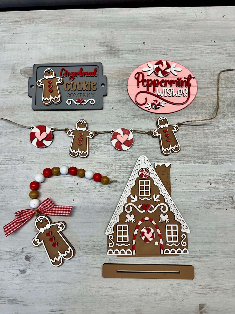 K&ouml;nnte beinhalten: Weihnachtsdekorationen zum Thema Lebkuchen, darunter ein Lebkuchenhaus, ein Lebkuchenmann-Anh&auml;nger, ein Banner mit Lebkuchenm&auml;nnern und Zuckerstangen sowie ein Schild mit der Aufschrift "Gingerbread Cookie Company".
