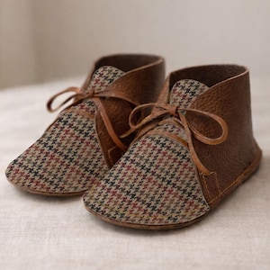 May include: A pair of ankle boots featuring a textured brown leather heel and side panels combined with a multi-colored houndstooth fabric toe and tongue. The boots are secured with thin brown leather laces tied in a bow at the front.