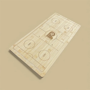 May include: A rectangular bamboo cutting board with an engraved hockey rink design. The board features a center ice logo and face-off circles. The light brown board has a recessed edge and is set against a neutral background.