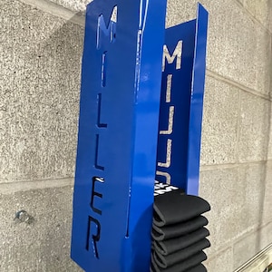 May include: Blue metal wall mounted storage rack with the word "MILLER" cut out. The rack is holding a stack of black socks.
