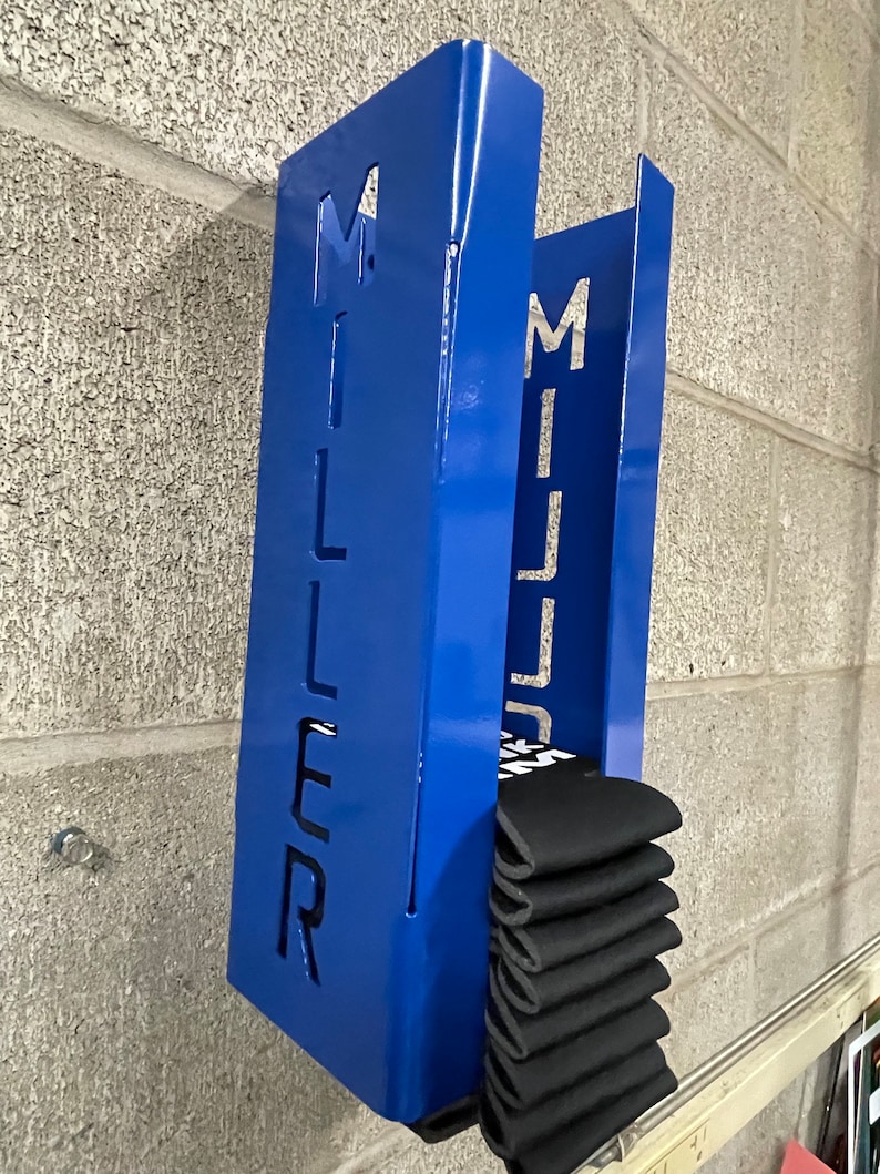 May include: Blue metal wall mounted storage rack with the word "MILLER" cut out. The rack is holding a stack of black socks.