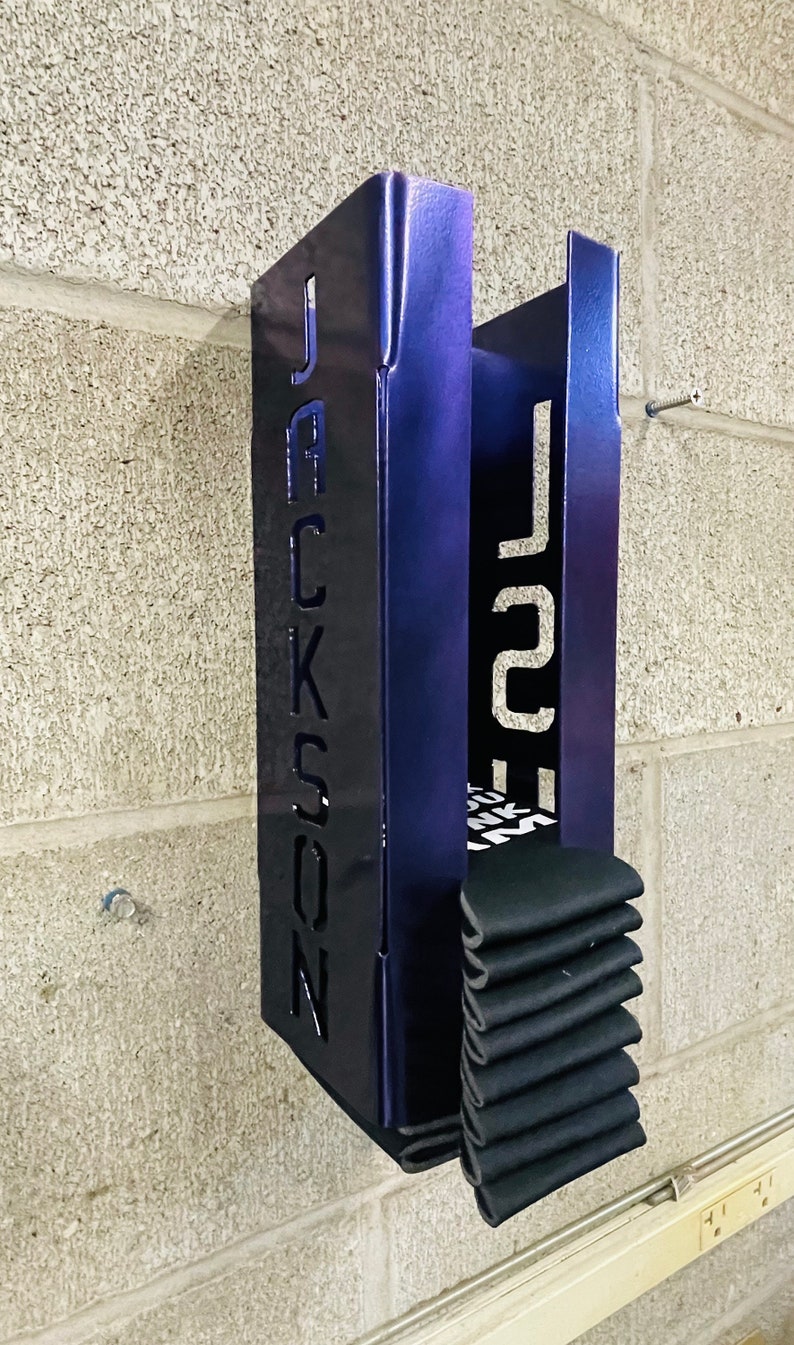 May include: A metal wall-mounted storage rack with the name "JACKSON" cut out on the front. The rack is painted a dark blue color and has a stack of black socks inside.