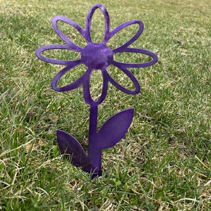 May include: Purple metal daisy flower garden stake. The flower has a simple design with rounded petals and a center circle. The stem has two leaves.