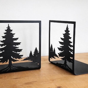 May include: Black metal bookends featuring a cut-out forest scene with pine trees. The bookends are rectangular with a base for stability. The design is a silhouette of trees and a landscape.