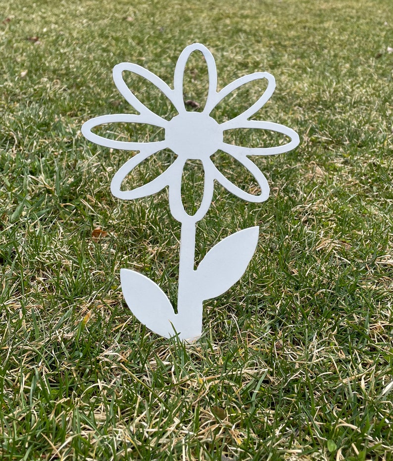 May include: White metal daisy flower garden stake with a simple design. The stake is inserted into the ground and features a stylized flower with a stem and leaves.