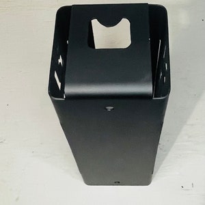 May include: Black metal wall mounted holder with a rectangular shape and a cut-out for a roll of paper towels.