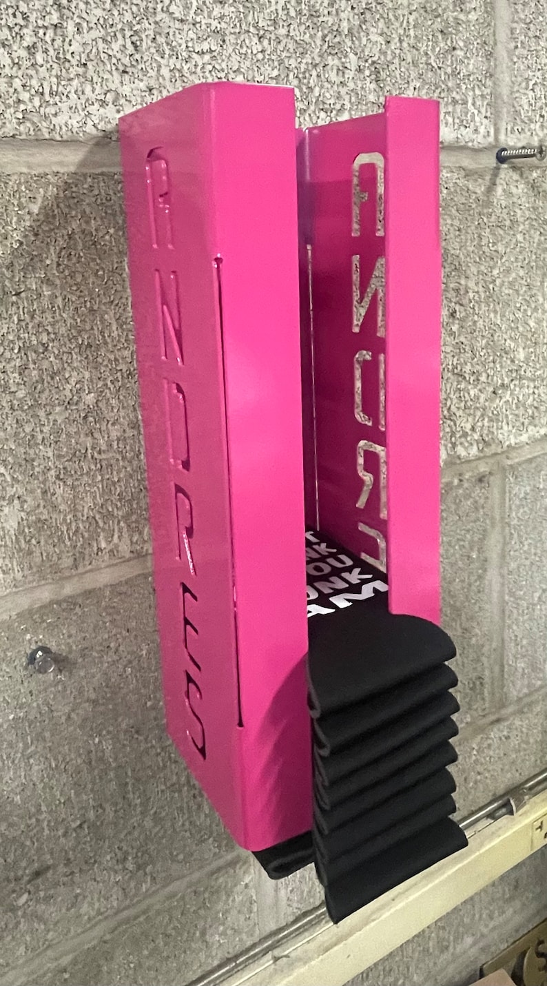 May include: Pink metal wall mounted organizer with the word "PINK" on the right side and "DREES" on the left side. The organizer is holding a stack of black socks.