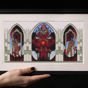 May include: Framed cross-stitch artwork depicting a gothic design with a central red demon figure and flanking figures in red and brown. The artwork is set against a backdrop of arched windows and a blue sky, framed in a black frame.