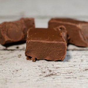 May include: Three pieces of chocolate fudge, two are rectangular and one is a smaller, irregular shape. The fudge is a rich brown color and has a slightly glossy surface.