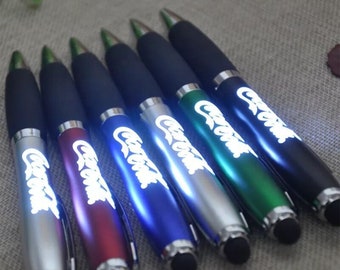 May include: Seven colorful pens with a light-up feature and a stylus tip. Each pen has the word "Coca-Cola" printed on it in white.