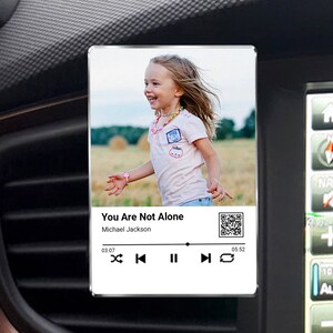 May include: A white digital music player with a photo of a young girl in a pink shirt running in a field. The player displays the song title "You Are Not Alone" by Michael Jackson. The player has controls for play, pause, skip forward, skip back, and repeat.