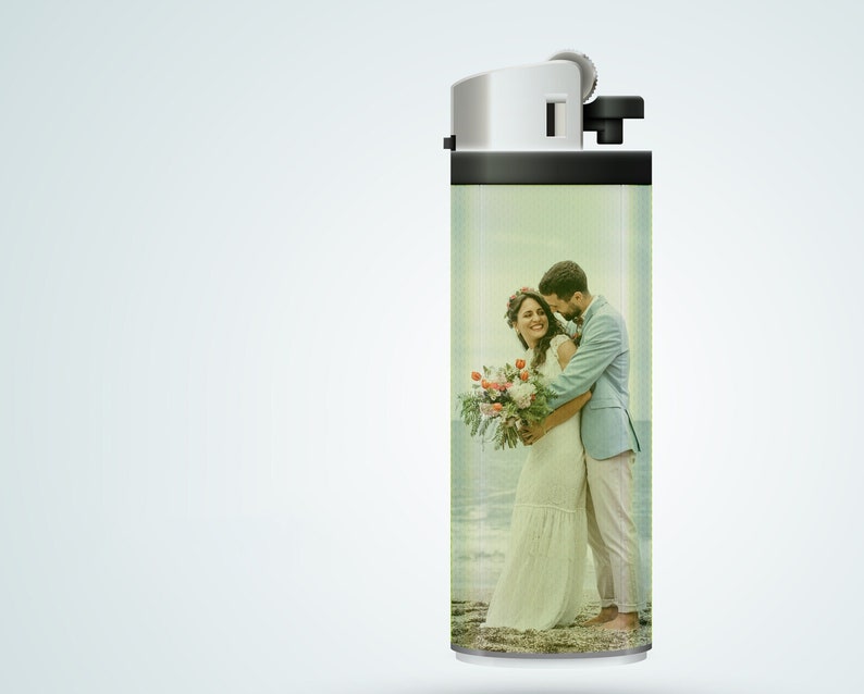 May include: A white lighter with a black top and a photo of a couple on the side. The photo shows a man and a woman in wedding attire, embracing on a beach.