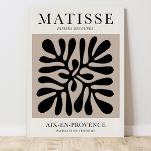 May include: A beige poster with black text that reads "MATISSE PAPIERS DÉCOUPÉS" and "AIX-EN-PROVENCE PAVILLON DE VENDÔME". A black abstract design of leaves is in the center of the poster.