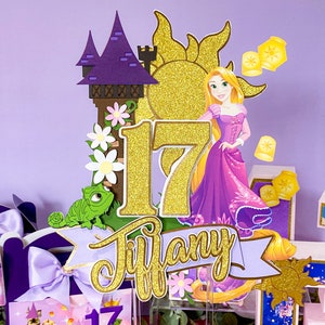 May include: A purple and gold cake topper featuring Rapunzel from the Disney movie Tangled. The topper includes a tower, a sun, a number 17, and the name "Tiffany".