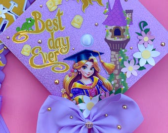 May include: Purple graduation cap decorated with a Rapunzel theme. The cap features a purple glitter background, a gold glitter sun, a purple tower, a Rapunzel character, and a purple bow with gold accents. The text "Best day ever" is written in gold glitter on the cap.