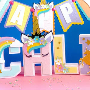 May include: A set of colorful, 3D letters spelling "CALI" decorated with a unicorn, rainbow, and stars. The letters are made of cardboard and have a glittery finish.
