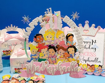 Può includere: Un topper per torta rosa e argento con un design a castello e le parole "Happy 1st Birthday". Il topper presenta un gruppo di personaggi di principesse Disney, tra cui Ariel, Belle, Cenerentola e Biancaneve. Il topper include anche uno stendardo rosa con il nome "Mia Raphaella".