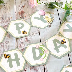 May include: A green and yellow honeycomb patterned banner with the word "Happy" spelled out in green letters. Each letter is on a separate hexagon-shaped card with a small bee illustration. The banner is strung together with white ribbon.