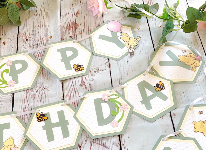 May include: A green and yellow honeycomb patterned banner with the word "Happy" spelled out in green letters. Each letter is on a separate hexagon-shaped card with a small bee illustration. The banner is strung together with white ribbon.