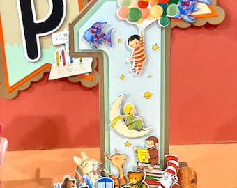 Può includere: Una grande decorazione tridimensionale a forma di numero uno con vari ritagli di personaggi delle fiabe, tra cui un bambino con palloncini, una figura su una luna crescente e una scimmia che legge un libro. La base mostra il nome LEVI in grassetto.