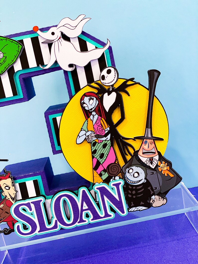 K&ouml;nnte beinhalten: Ein dreidimensionaler Kuchentopper in Form der Zahl drei, in den Farben Lila und T&uuml;rkis, auf einem schwarz-wei&szlig; gestreiften Hintergrund. Der Topper zeigt Figuren aus dem Film Nightmare Before Christmas, darunter Jack Skellington, Sally und Oogie Boogie. Der Topper enth&auml;lt auch den Namen "SLOAN" in lila und t&uuml;rkisfarbenen Buchstaben.