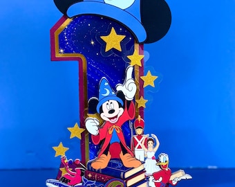 Può includere: Un topper per torta a forma di numero uno realizzato in carta a strati, con un cappello da mago blu decorato con stelle e una luna, un personaggio centrale di Topolino e figure più piccole tra cui un soldato, una ballerina e un papero. Il nome SHILOH è stampato alla base.