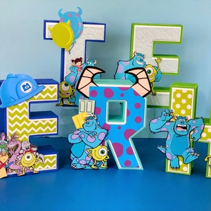 May include: A set of five colorful cardboard letters spelling "ERH" decorated with characters from the movie Monsters Inc. The letters are decorated with green and yellow polka dots, blue and purple polka dots, and green and yellow chevron patterns.