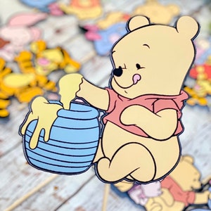 May include: A yellow cartoon bear character with a red shirt is holding a blue and white striped honey pot. The bear has a tongue sticking out and is looking at the honey pot.