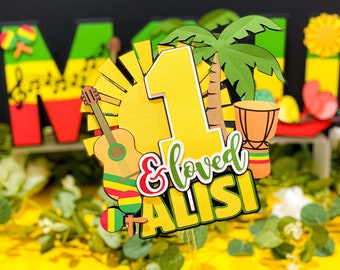 Op de afbeelding: Een gele en groene taarttopper met een groot nummer één, een gitaar, een palmboom, een trommel en de tekst "& loved ALISI".