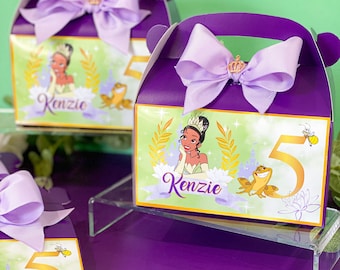 May include: Purple favor boxes with a green and gold design featuring a cartoon princess, a frog, and the number 5. The boxes have a purple ribbon with a gold crown and the name "Kenzie" printed on them.